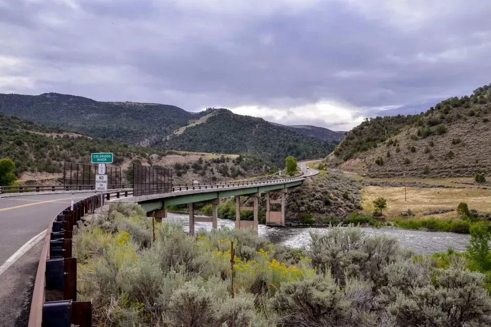 A bridge over a river in the middle of a valley with mountains in the background.