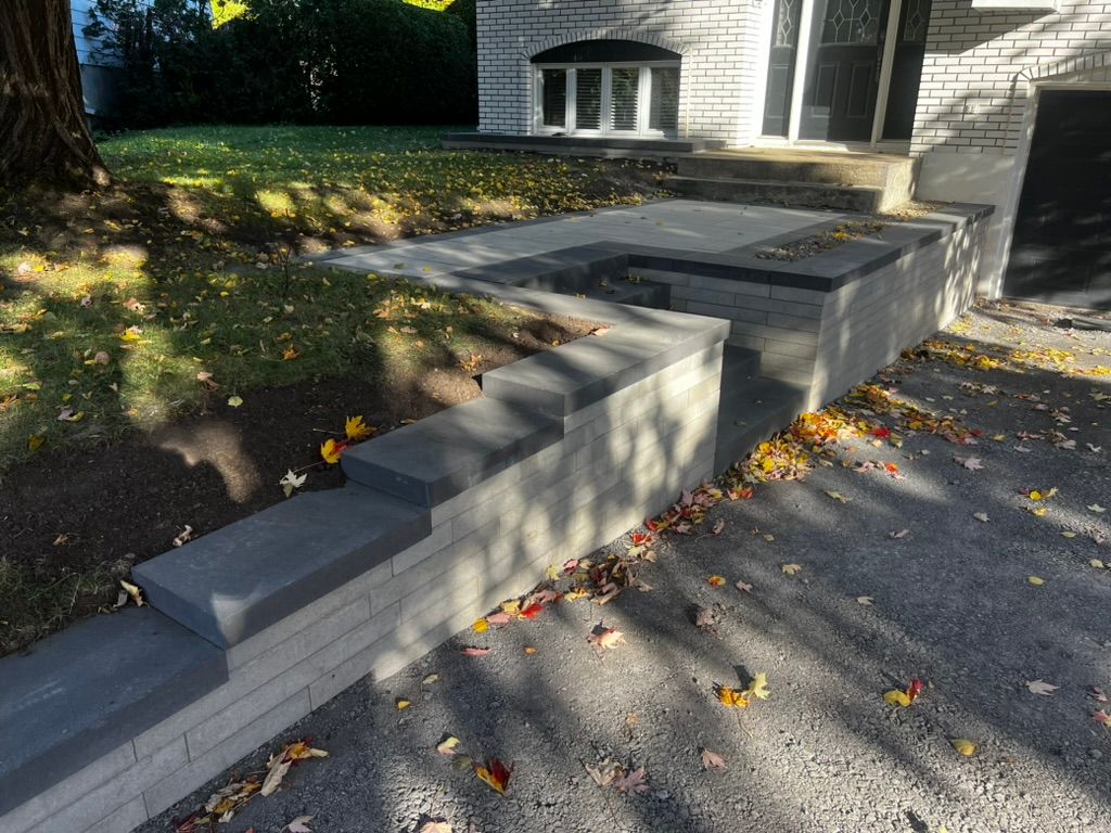 Brick retaining wall with steps leading to a house entrance. Autumn leaves scattered on the ground.