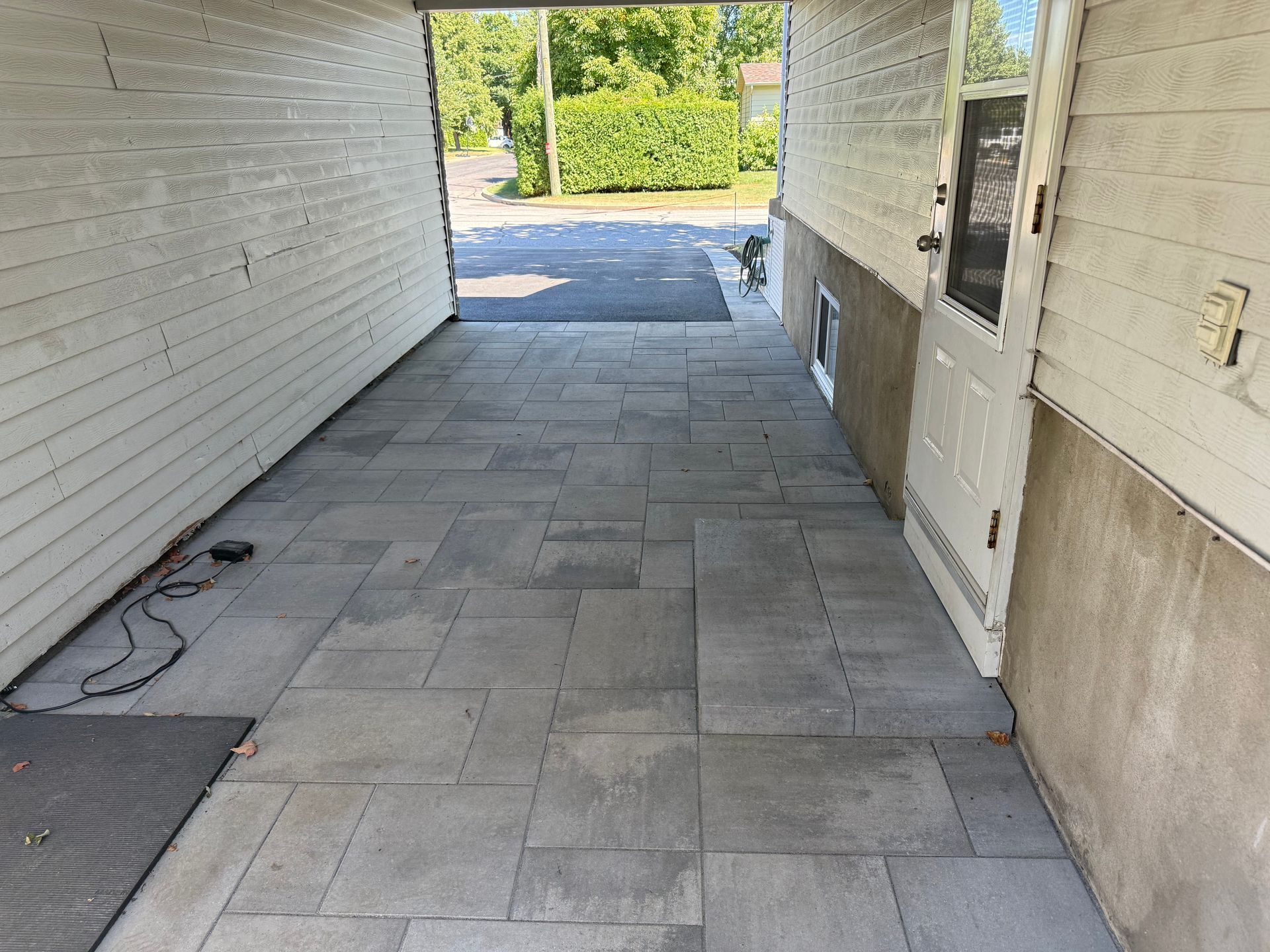 A covered entryway paved with gray stone. A white door is on the right, leading outside to a street.