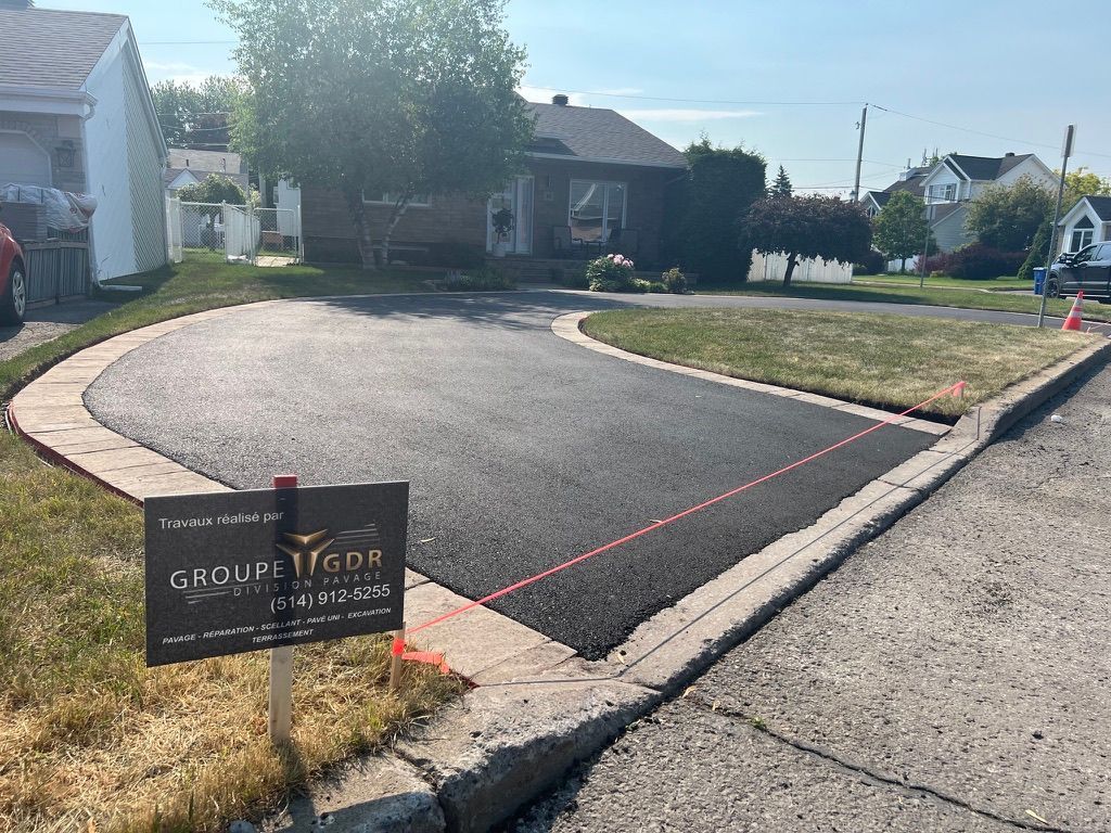 Newly paved asphalt driveway with stone border, in front of a house.