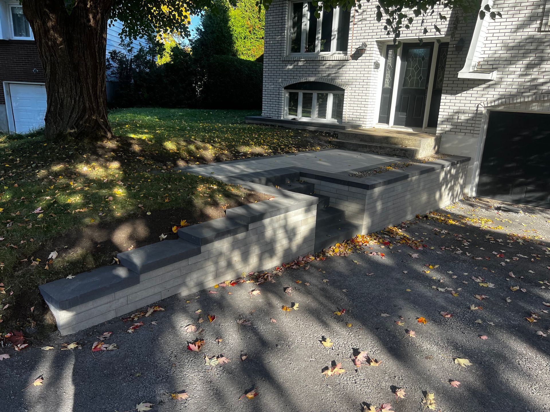 Concrete steps and walkway leading to a stone building entrance on a sunny day. Leaves litter the ground.