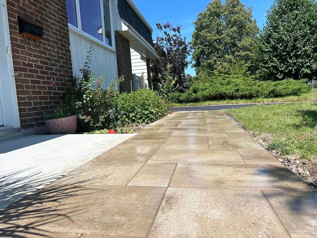 Stone walkway leading to a brick house on a sunny day. Green shrubs and lawn border the path.