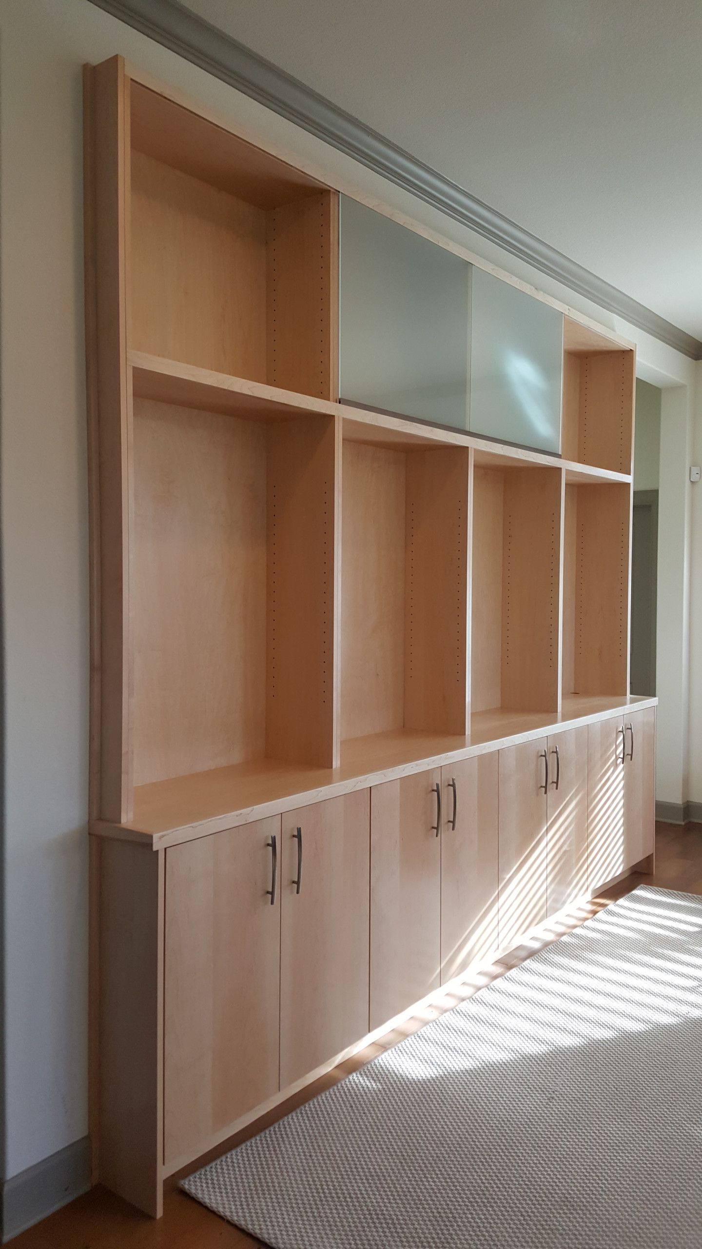 A living room with a long wooden bookshelf and cabinets.