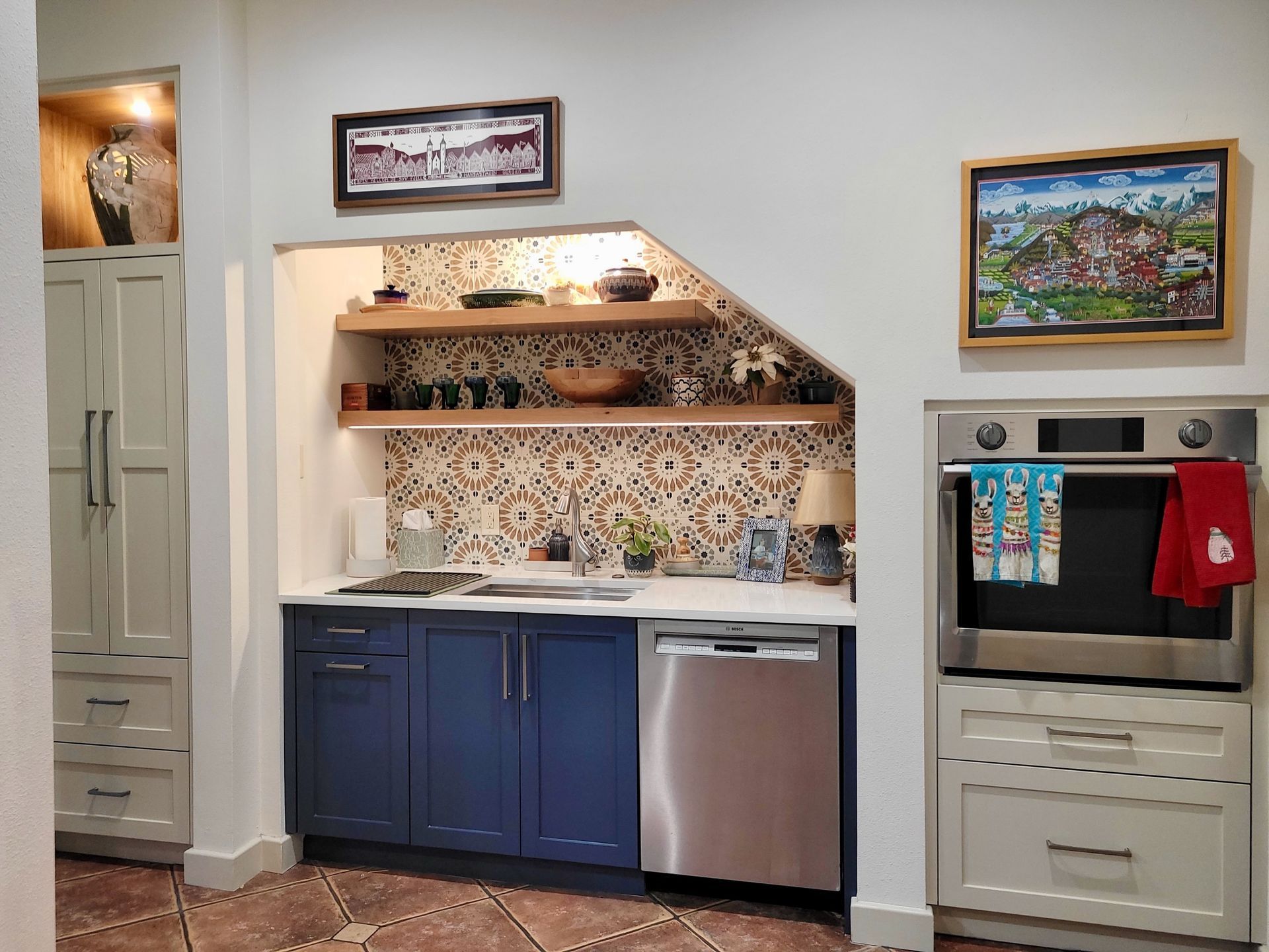 A kitchen with blue cabinets , a stainless steel dishwasher , and a painting on the wall.