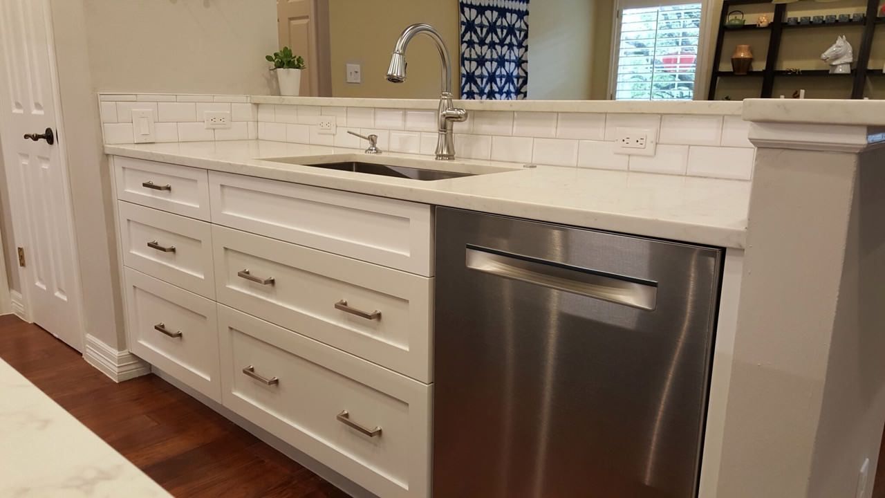 A kitchen with white cabinets , a sink , and a stainless steel dishwasher.
