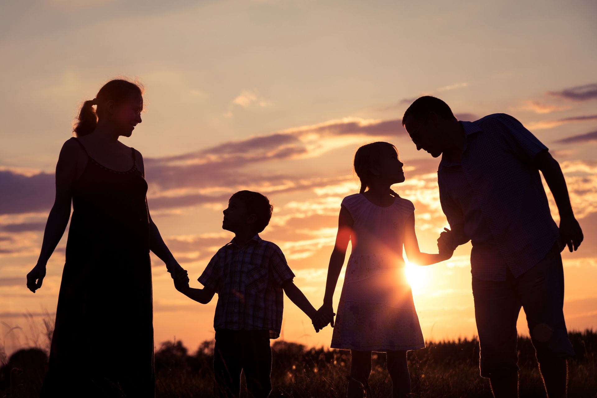 A family is holding hands in a field at sunset.