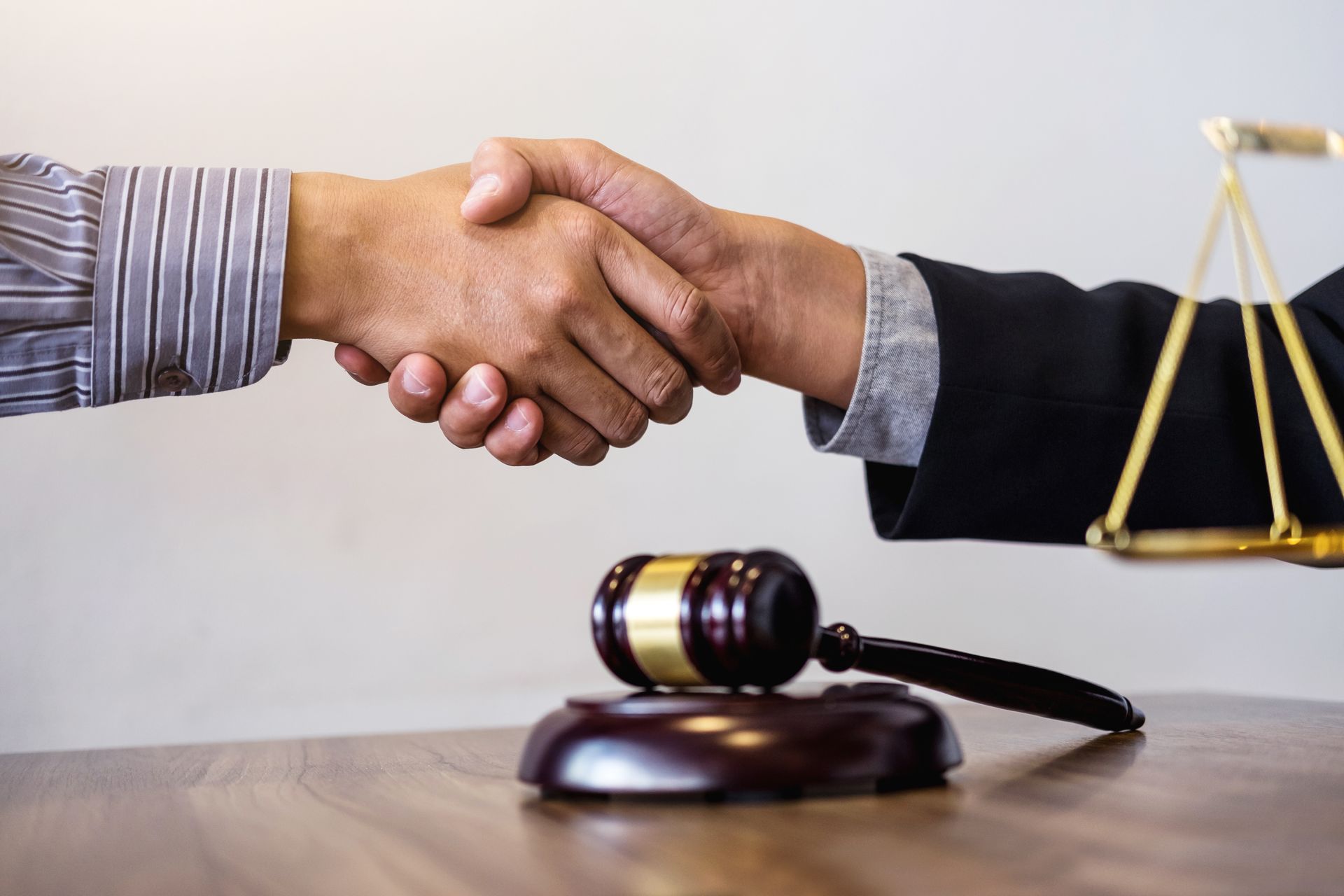 Two people shaking hands near a gavel, scales of justice, on a wooden table.