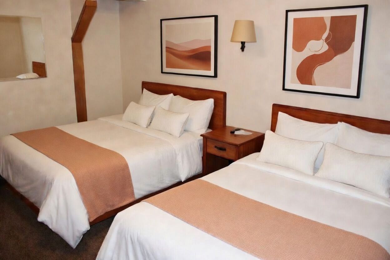 Hotel room with two white beds, peach accents, bedside table, and framed wall art