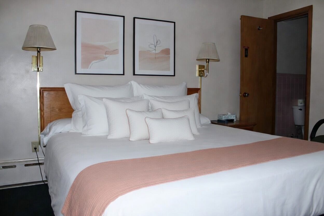 Neatly made bed with white and pale pink bedding in a hotel-style room