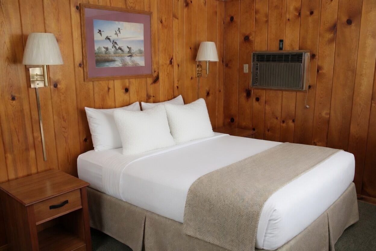 Cozy bedroom with wood-paneled walls, a white bed, nightstands, lamps, and a framed picture.