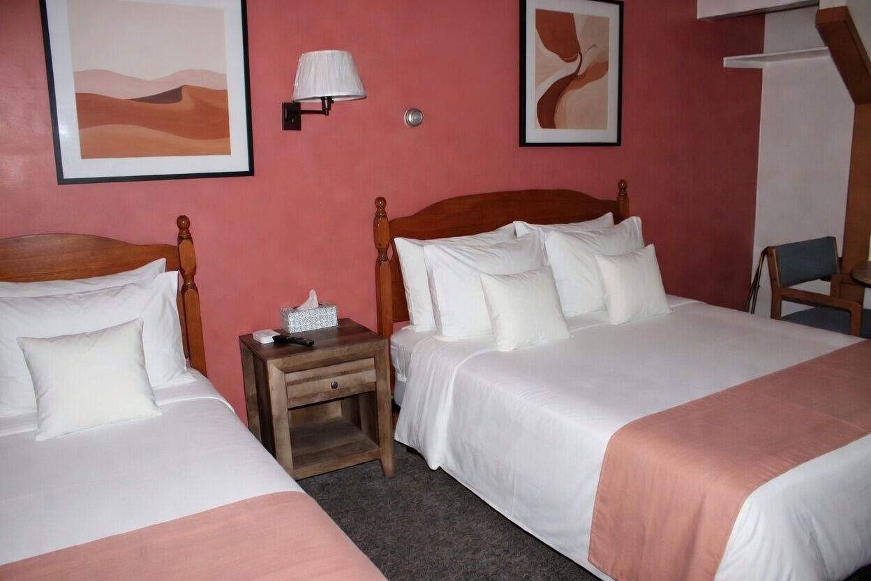 Hotel room with two neatly made twin beds, coral walls, and framed abstract art above the nightstands