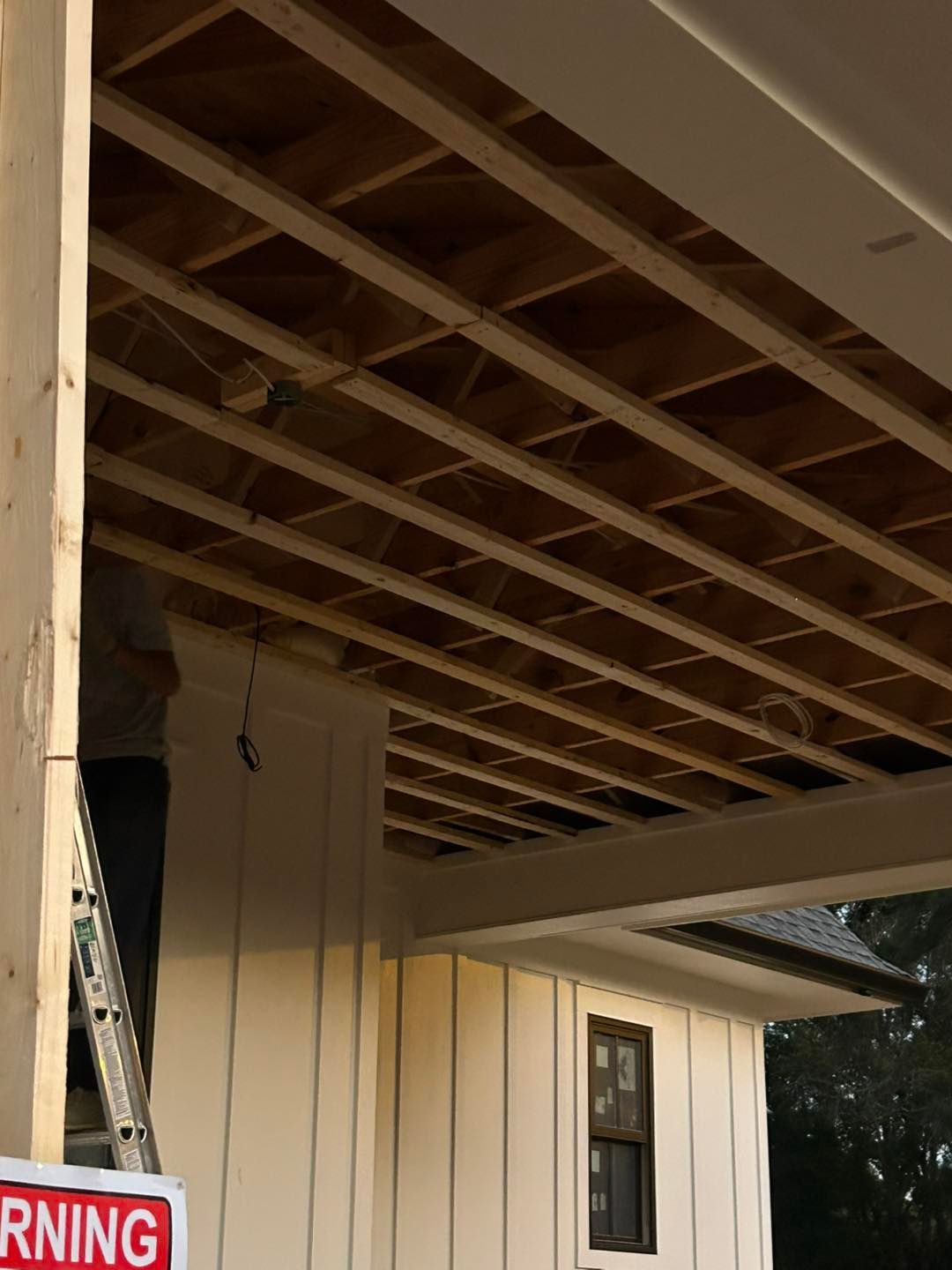 Construction site with exposed wooden beams, white siding, and a ladder.
