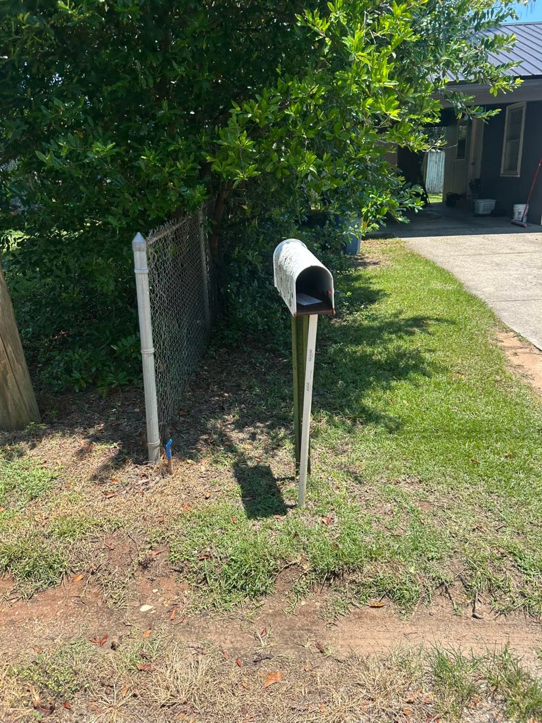 A silver mailbox on a wooden post beside a chain link fence and green grass.