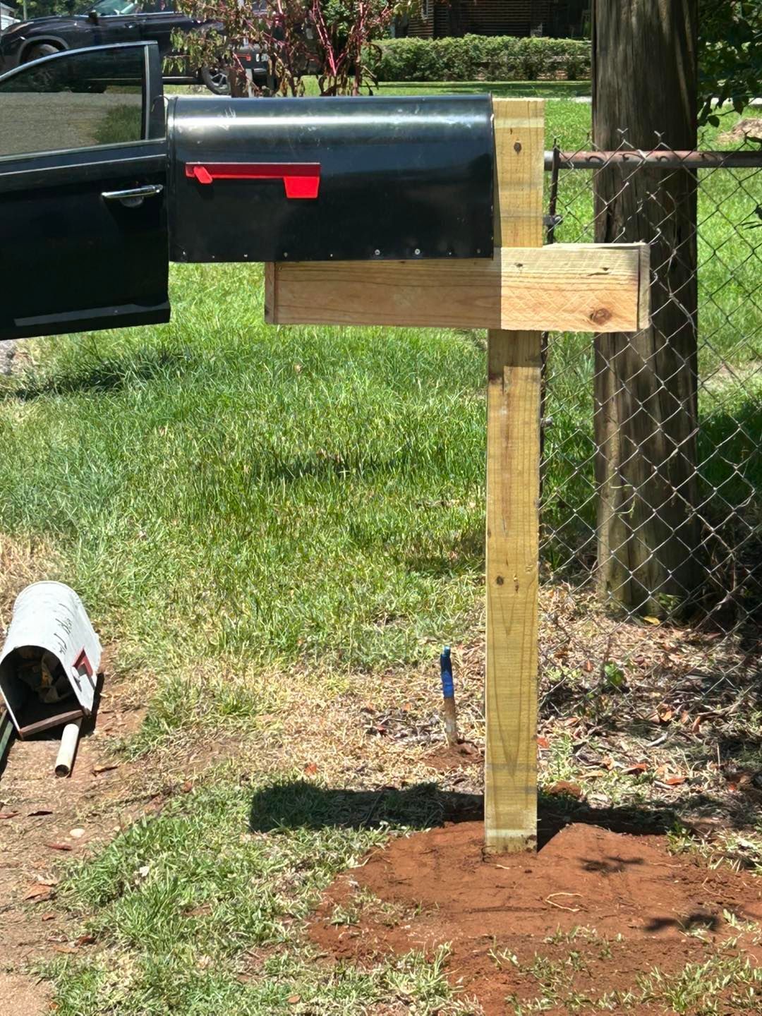 Mailbox on wooden post with a flag, beside a car door, in a yard.