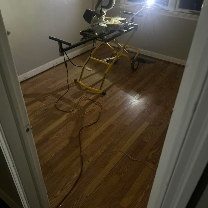 A small room with wood flooring, a yellow saw stand, and a miter saw.