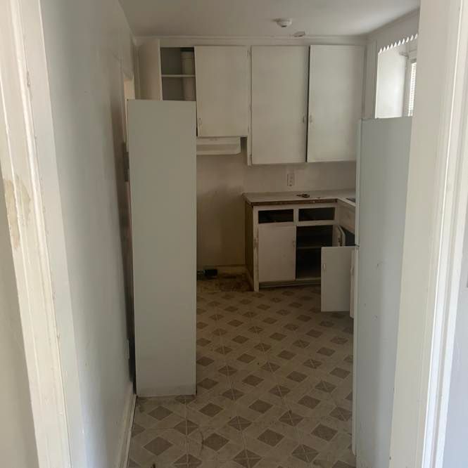 Empty kitchen with white cabinets, an open doorway, and patterned flooring.