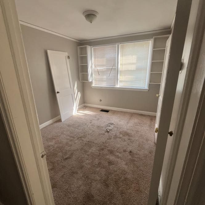 Empty room with carpet, built-in shelves by a window, and an open door.