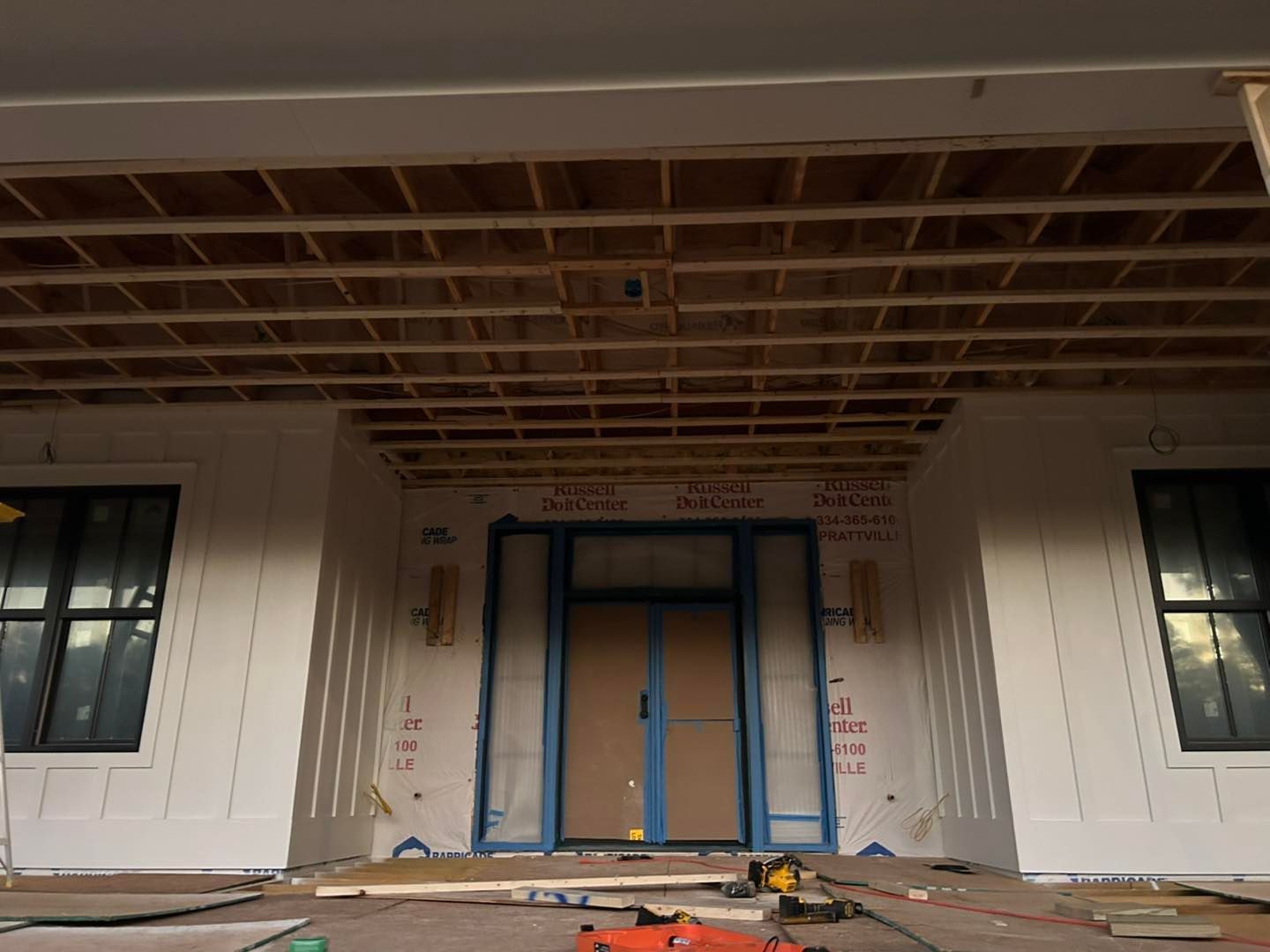 Exterior of a house under construction; wooden beams under a porch ceiling, doors and windows framed.