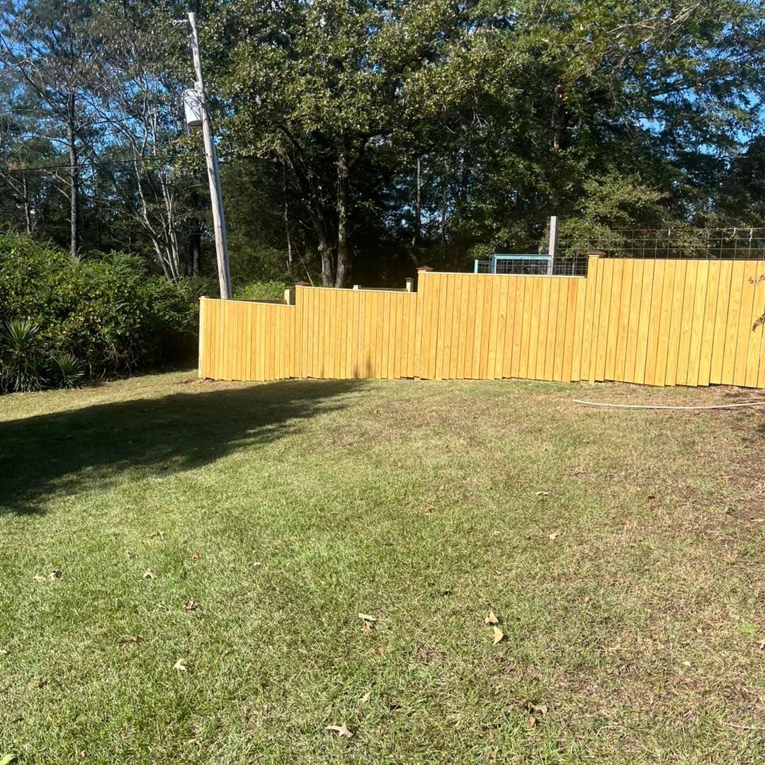Yellow wooden fence bordering a grassy backyard.