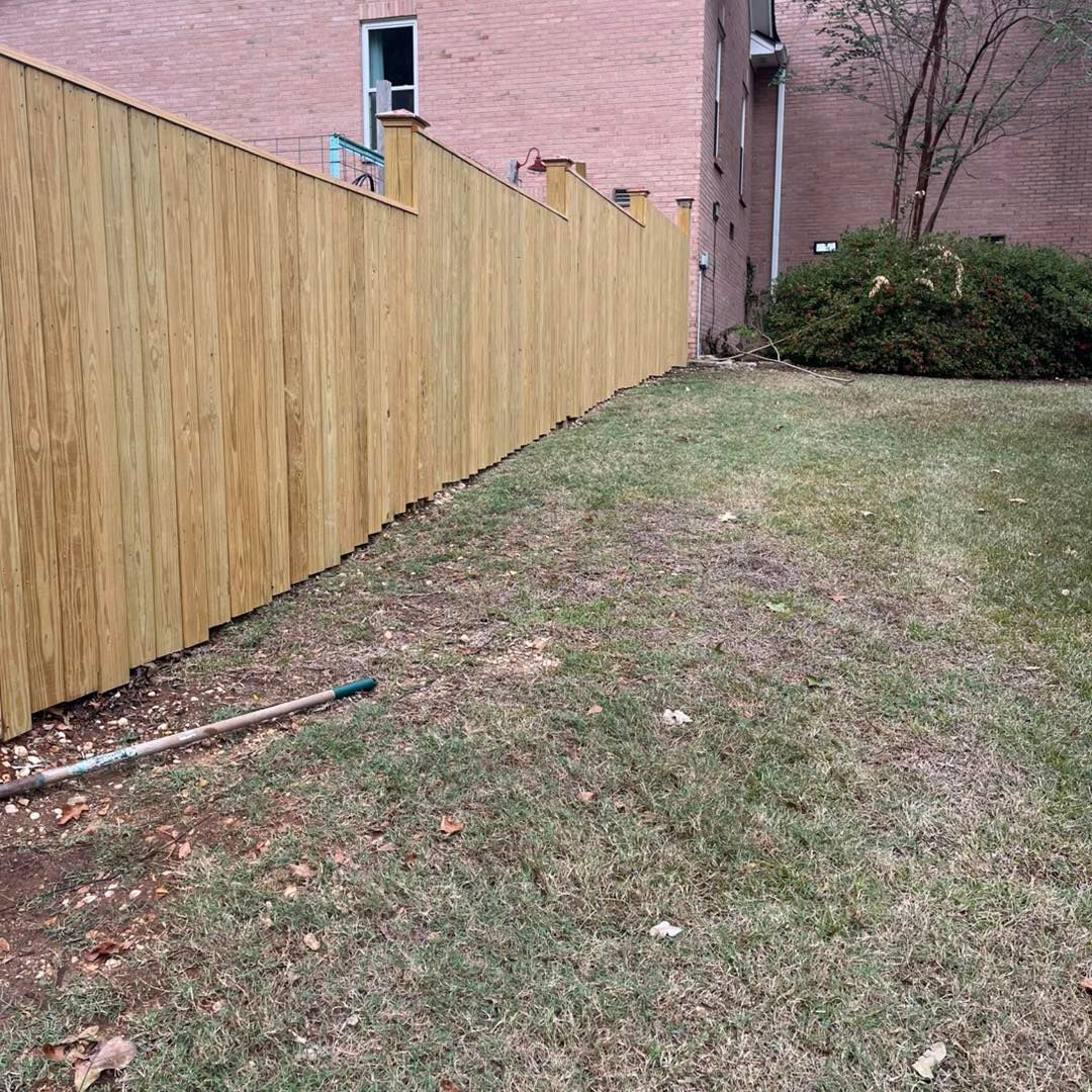 Wooden fence next to a patch of grass, next to a brick building.