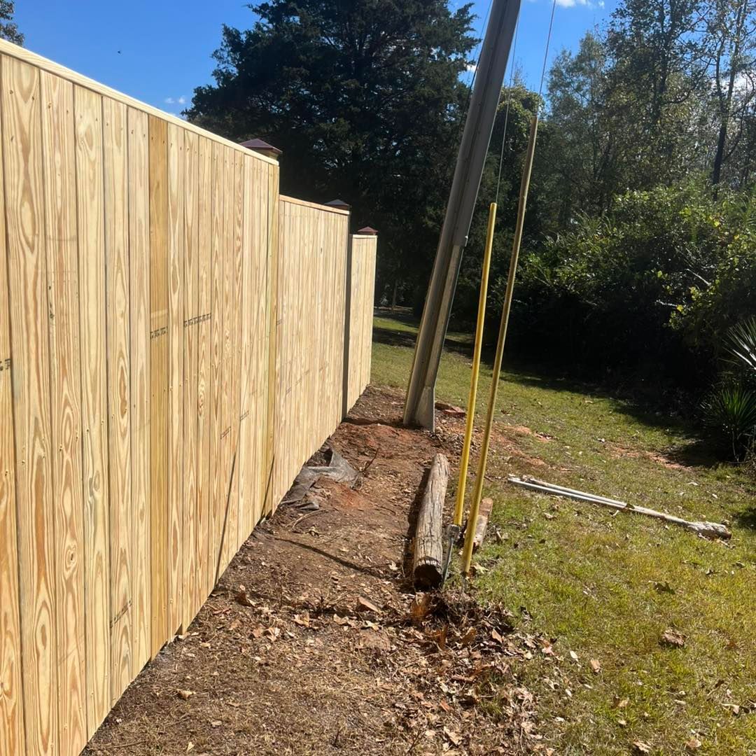 Wooden fence in a yard next to a utility pole and grassy area on a sunny day.