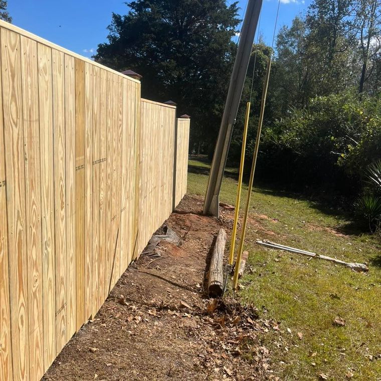 Wooden fence in a yard next to a utility pole and grassy area on a sunny day.
