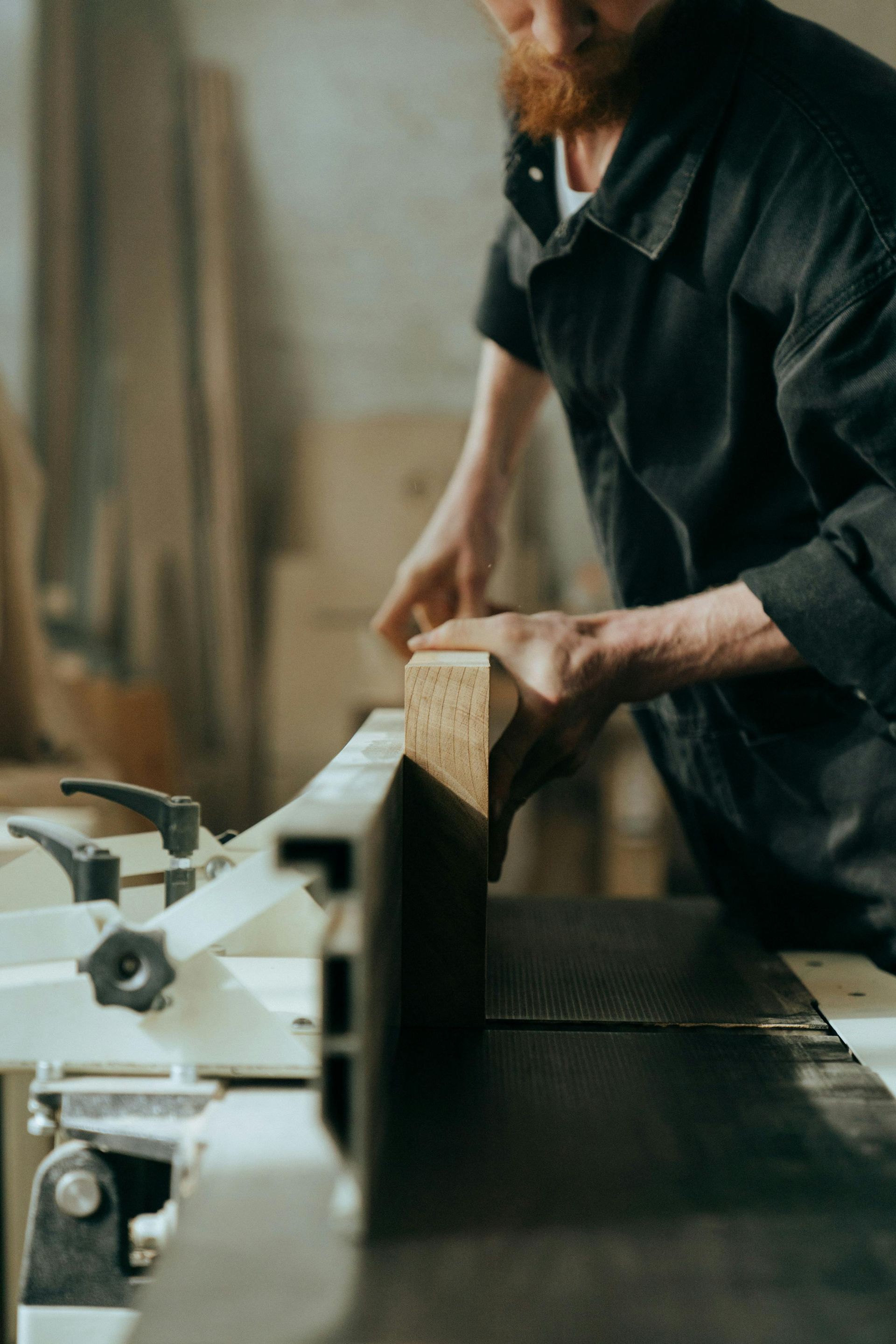 Carpenter operating a jointer, planing a wooden board in a workshop.