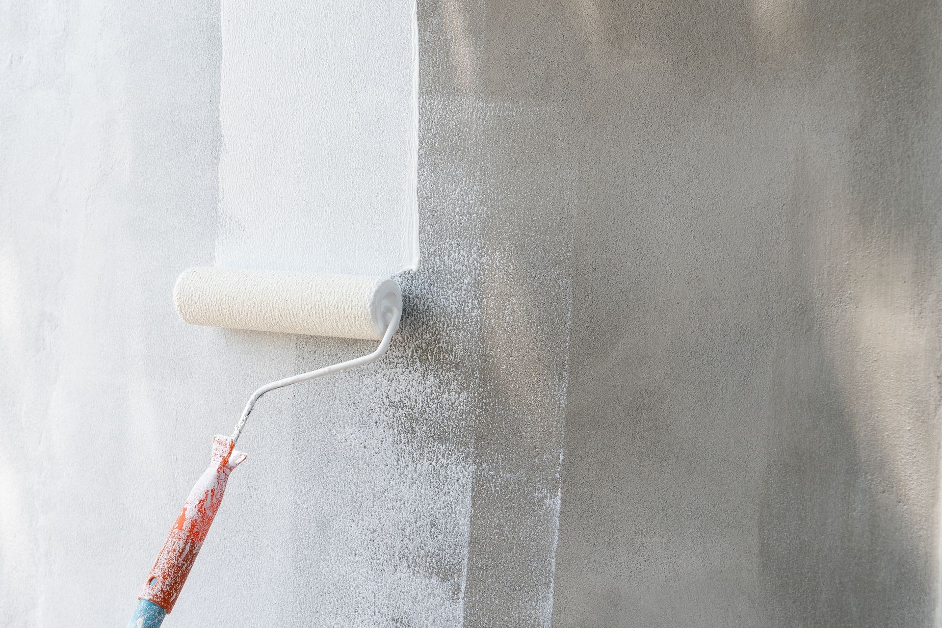 A paint roller applies white paint to a textured concrete wall, leaving a painted stripe.
