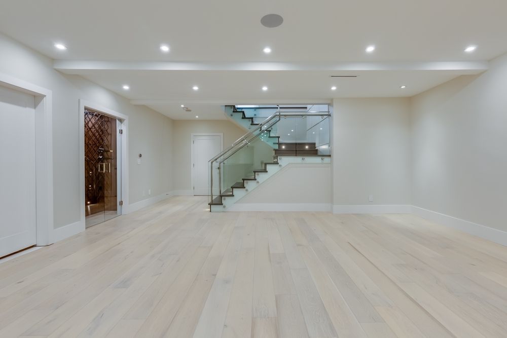 Spacious, light-flooded room with wood floors, stairs, and a wine cellar visible.