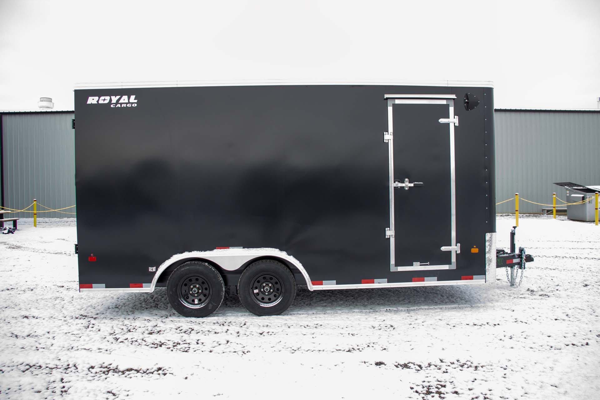 Black enclosed trailer with double wheels and side door, parked in snowy area.