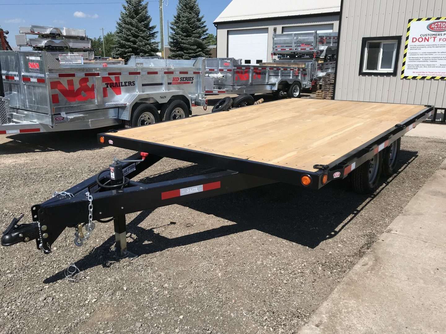 A black flatbed trailer with a wooden deck parked outside a building on a sunny day.