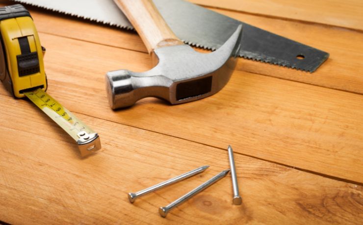 A set of carpentry tools including a tape measure, hammer, and saw on a wooden surface, representing deck repair services in Pomona, CA.