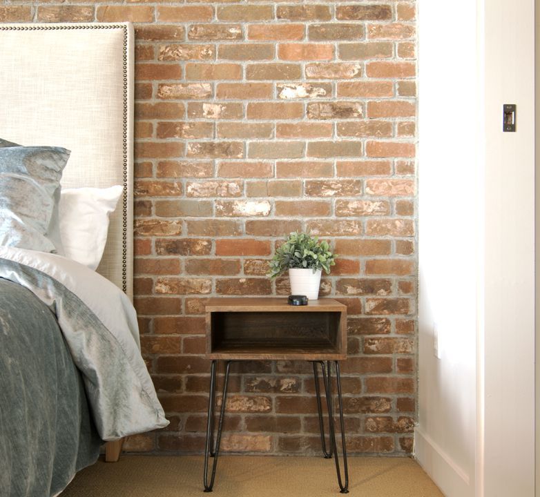 A bedroom with a brick wall and a nightstand