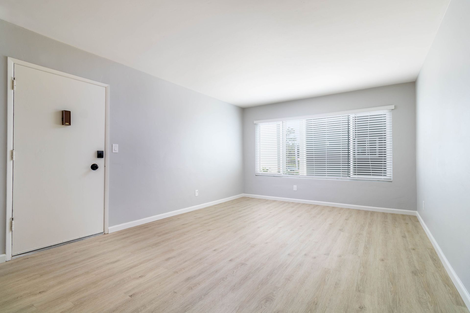 An empty living room with hardwood floors and a door.