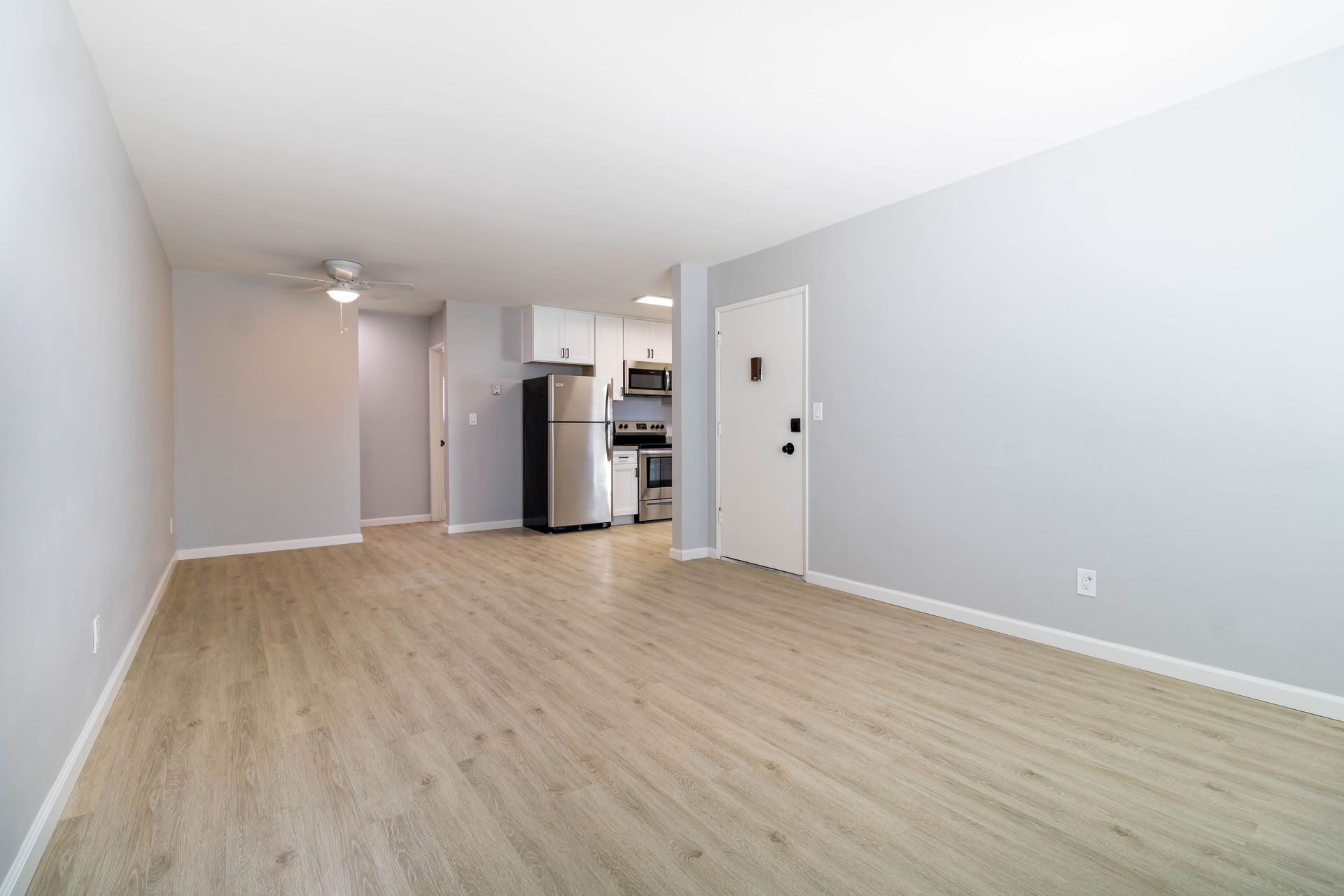 An empty living room with hardwood floors and a refrigerator.
