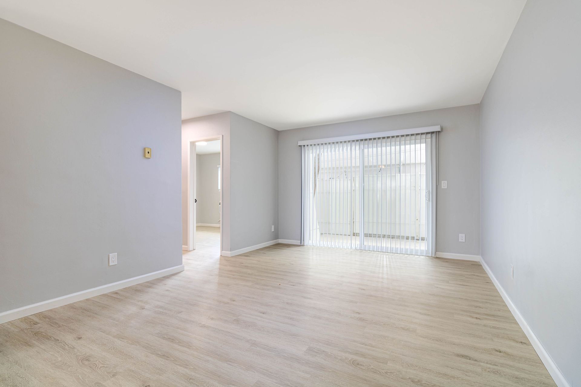 An empty living room with hardwood floors and sliding glass doors.