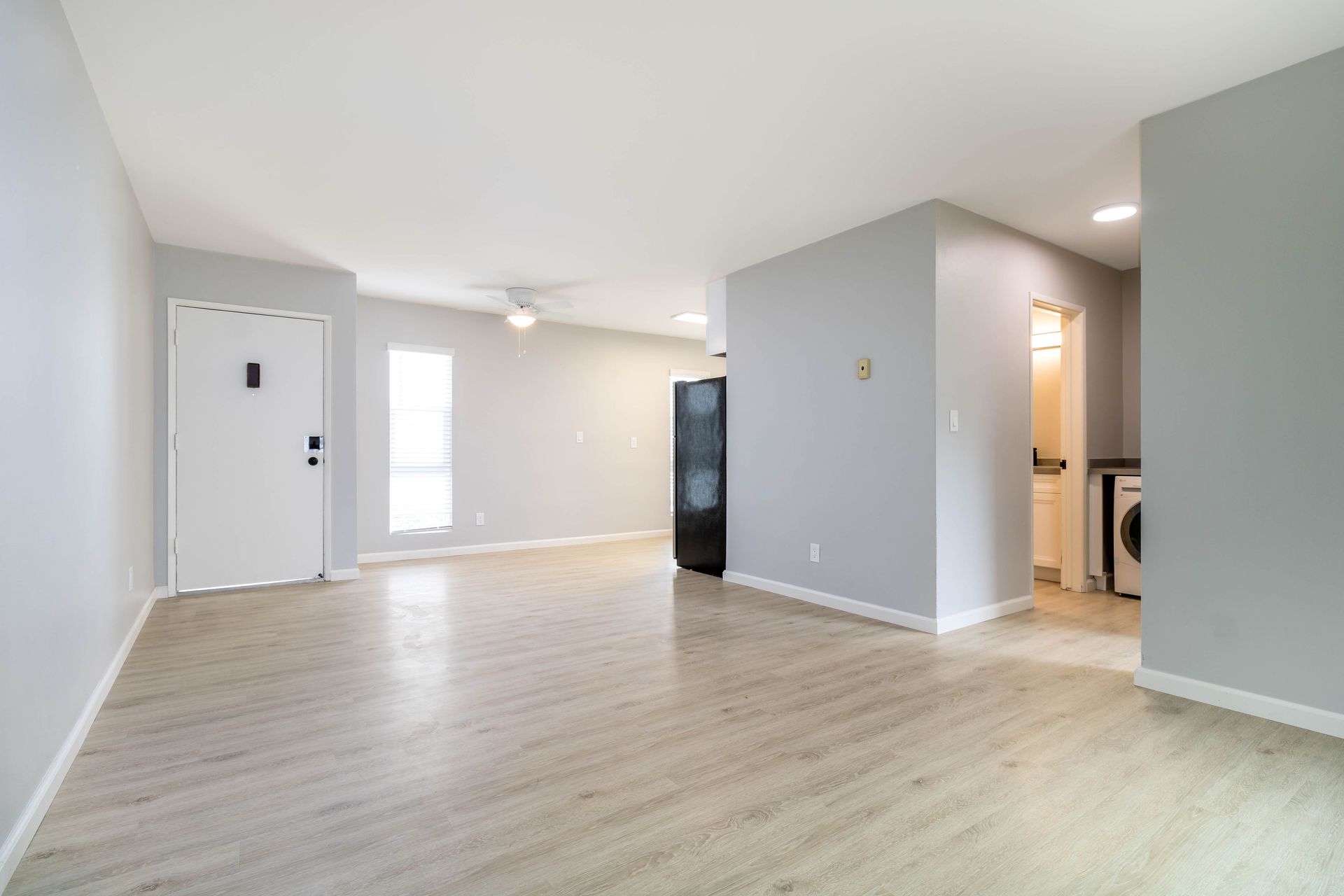 An empty living room with hardwood floors and a refrigerator.