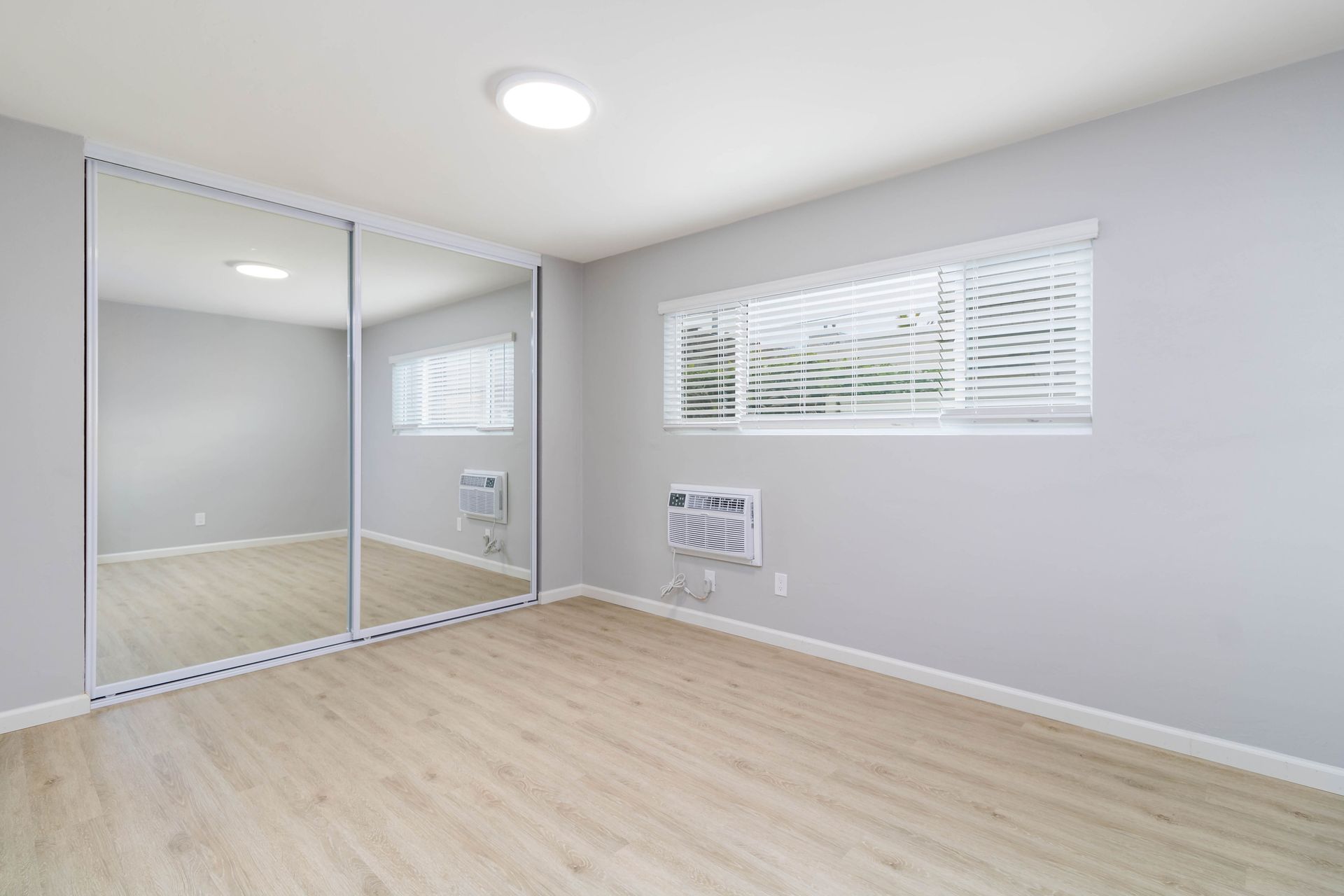 An empty bedroom with a large mirrored closet and a window.