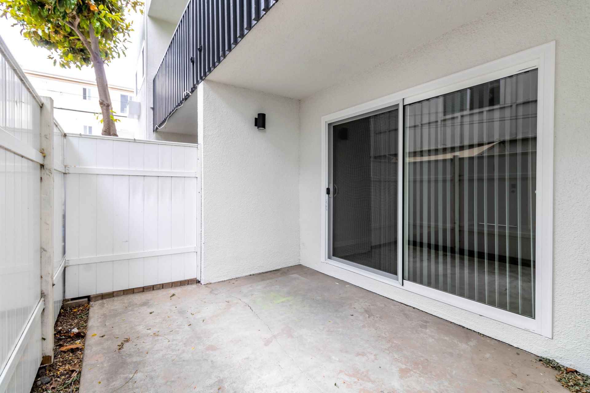 An empty patio with sliding glass doors and a white fence.