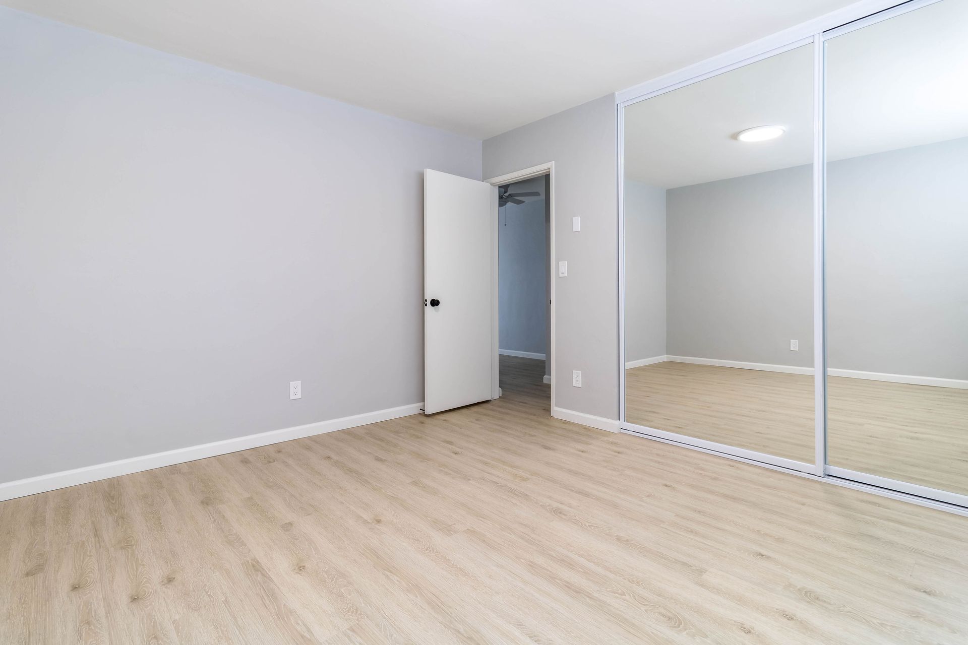 An empty bedroom with hardwood floors and sliding mirrored closet doors.