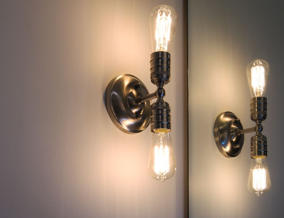 Two light bulbs are hanging on a wall next to a mirror.