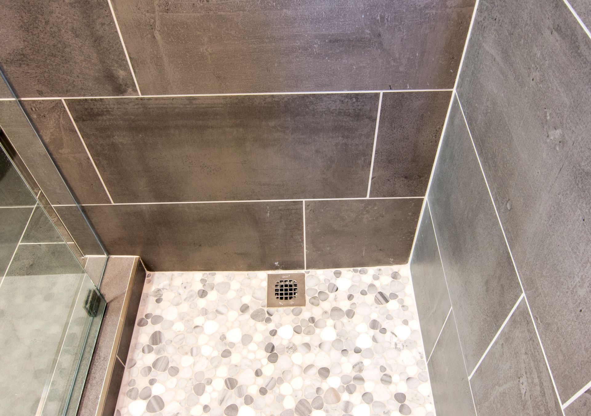 A bathroom with a walk in shower and a drain on the floor.