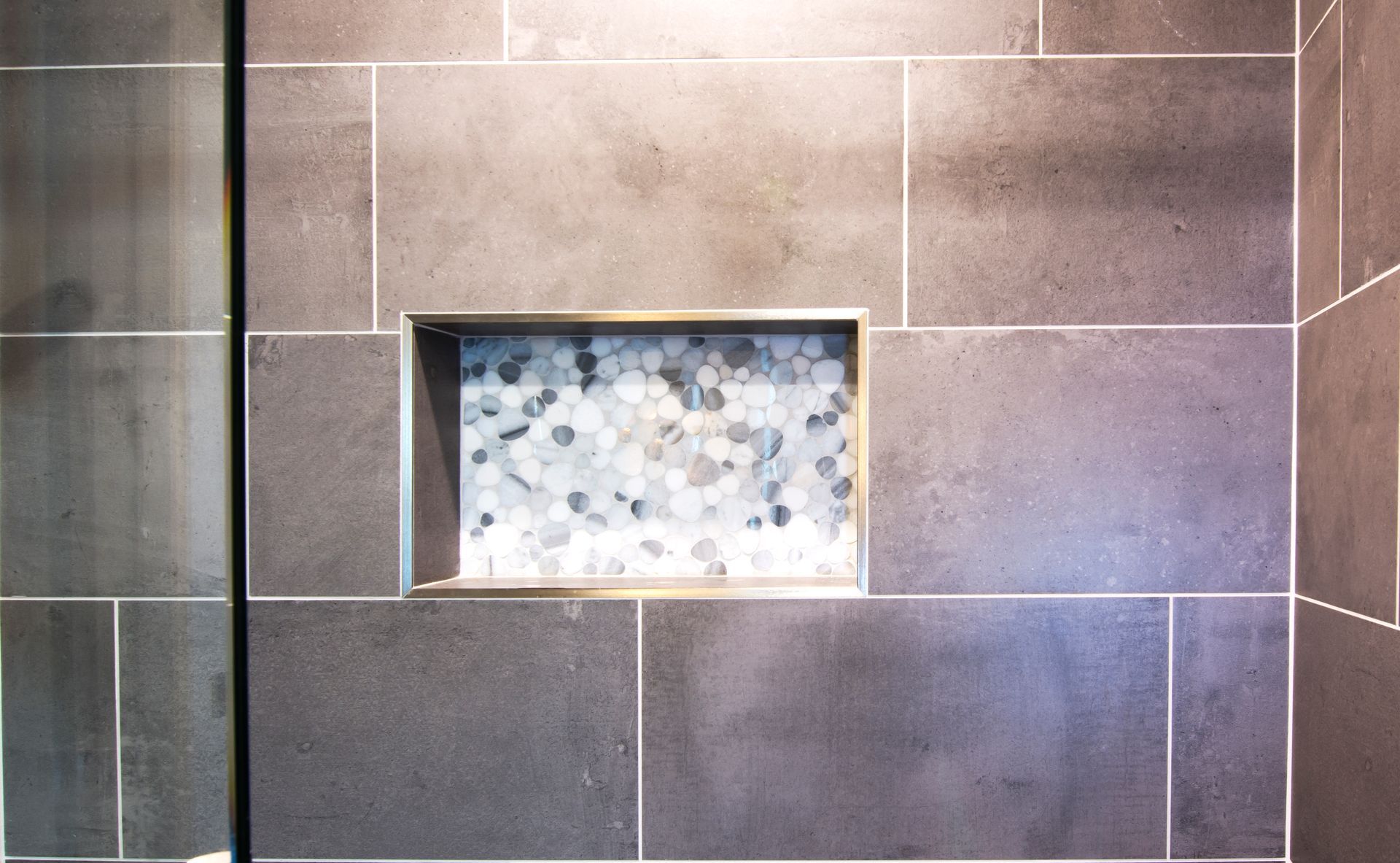 A shower with a tiled wall and a niche in the wall