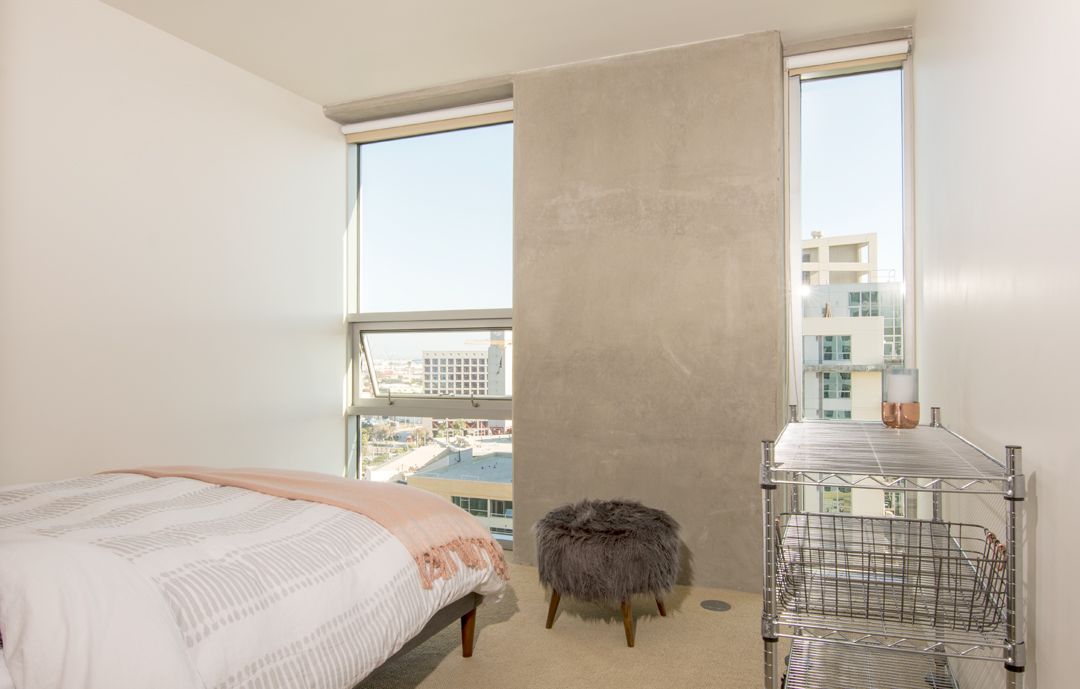 A bedroom with a bed , ottoman , and window.