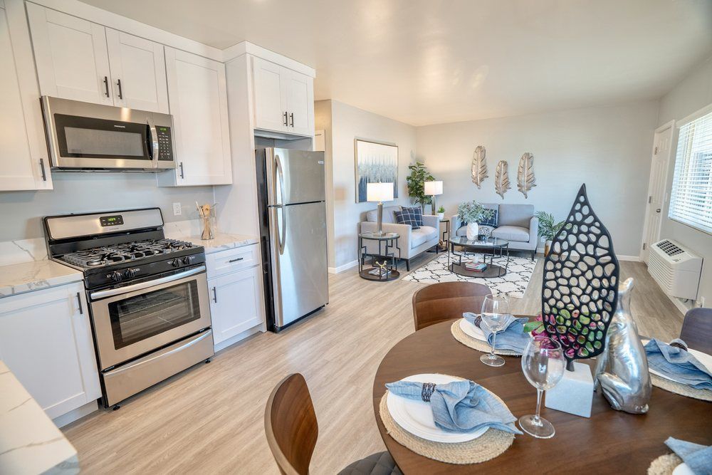 A kitchen with a stove , refrigerator , microwave , table and chairs.