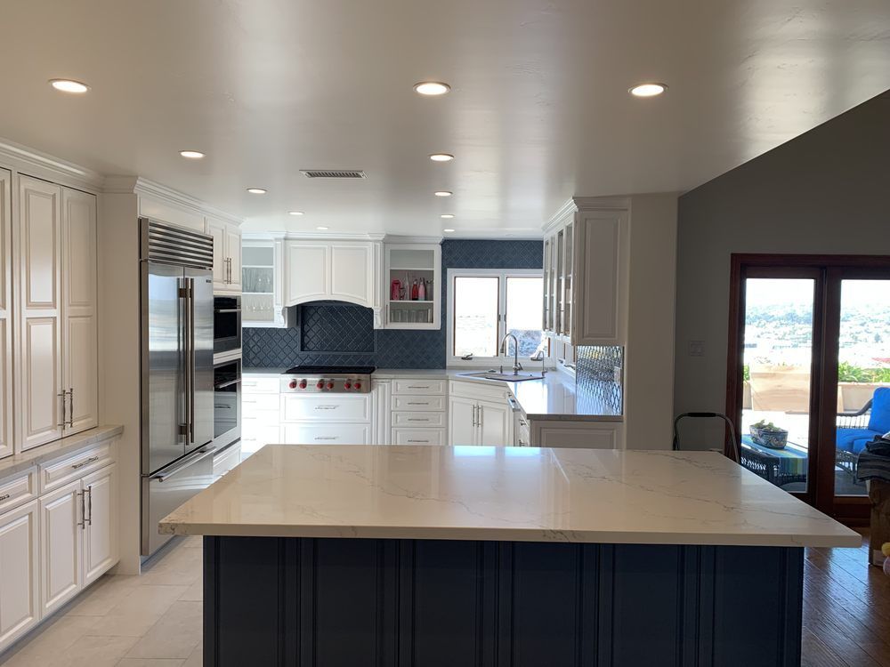 A kitchen with white cabinets , stainless steel appliances , and a large island.