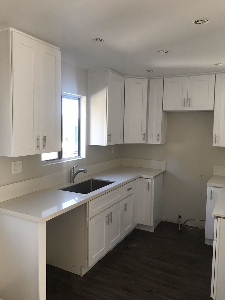 A kitchen with white cabinets , a sink , and a window.