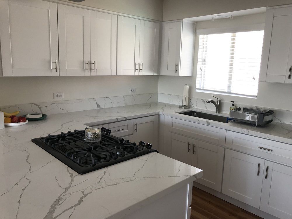 A kitchen with white cabinets , a stove top oven , a sink , and a window.