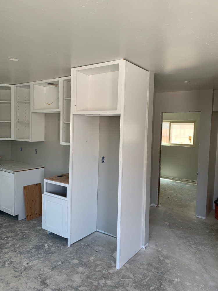 A kitchen under construction with white cabinets and a refrigerator.