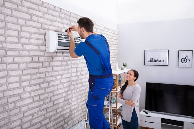 A man is installing an air conditioner on a brick wall in a living room.
